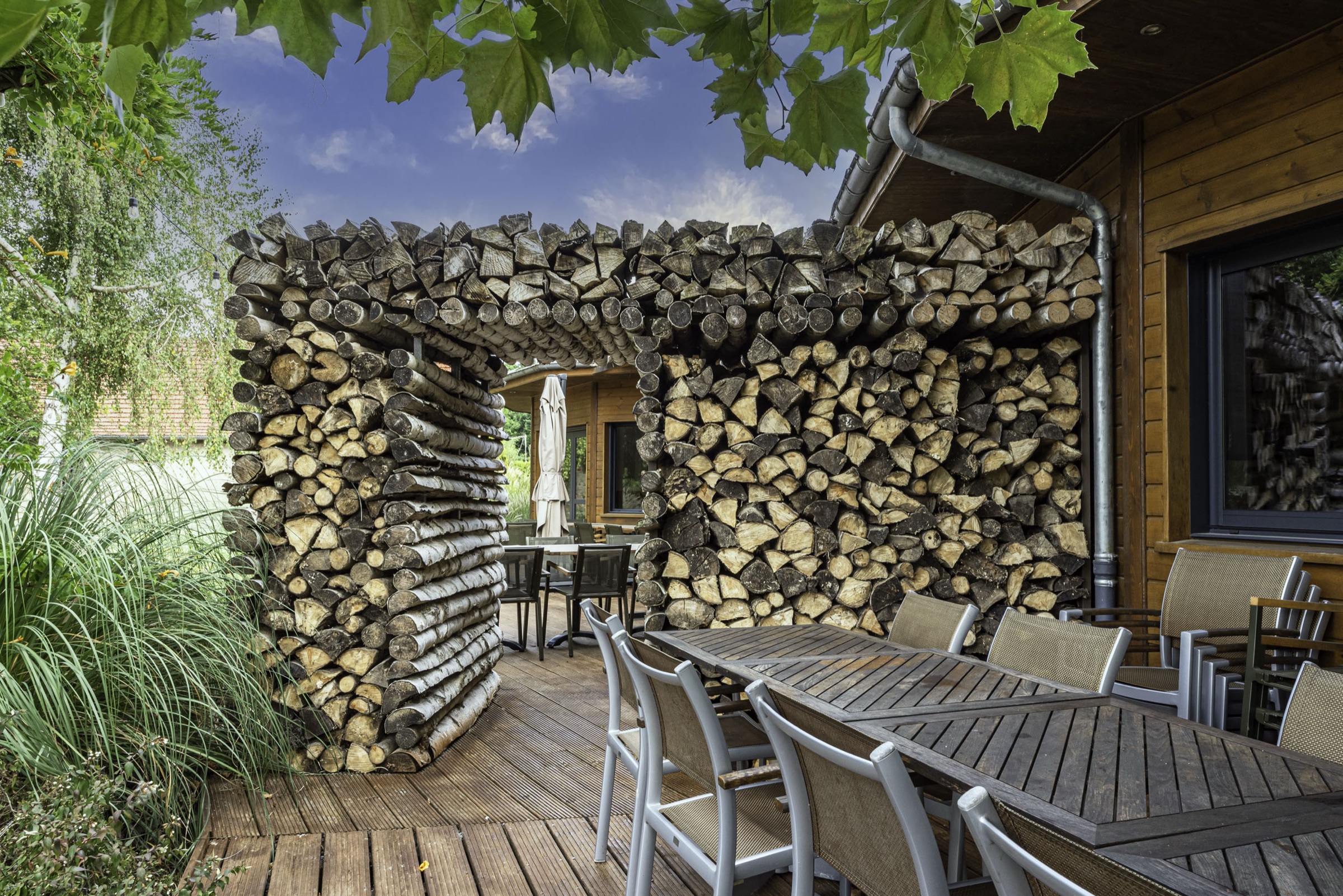 Terrasse en bois et mur de bûches du domaine des Étangs de l'Abbaye, dans la verdure